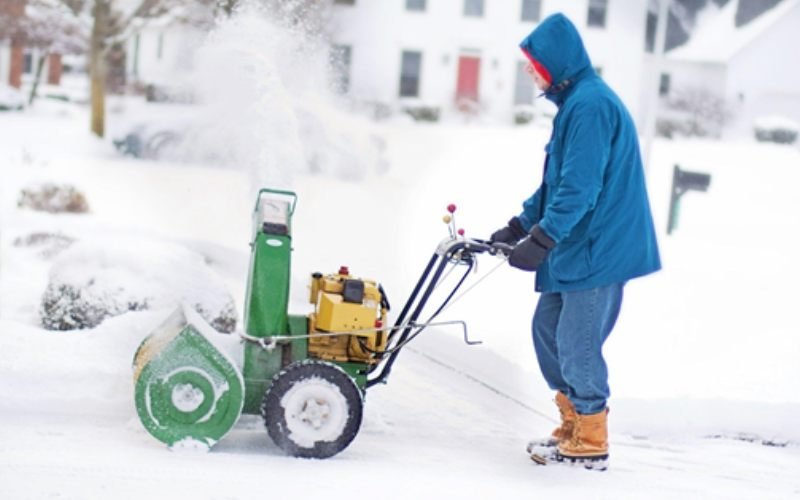 Person using a snow blower to clear snow from a residential driveway during winter.