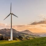 Wind turbine generating clean energy in a green mountain landscape at sunset.