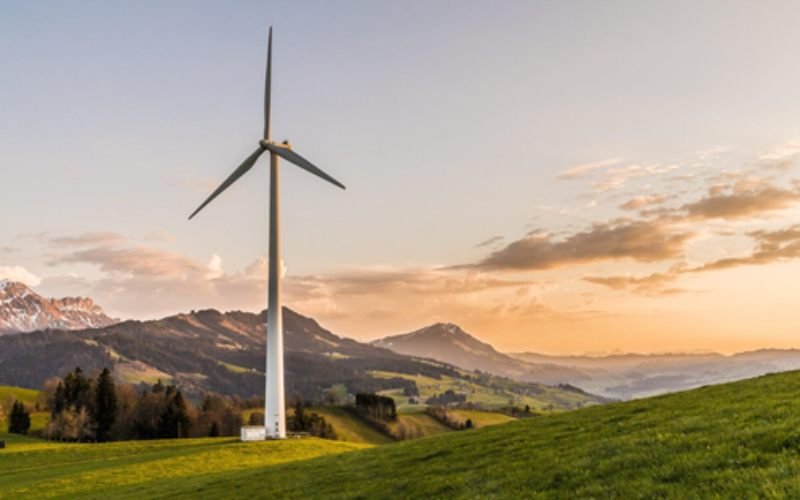 Wind turbine generating clean energy in a green mountain landscape at sunset.