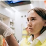 Healthcare trainee wearing a high-visibility vest and gloves carefully preparing a syringe inside an emergency medical vehicle.